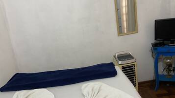 A hotel room with a bed, a massage chair, a massage table, a television, and a small table with a lamp.