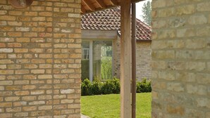 A brick building with a tiled roof, a wooden pergola, and a glass door leading to a green lawn. - B&B Het Weiland (Damme)