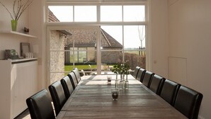 A dining room with a long table, black chairs, and a view of a garden through large windows. - B&B Het Weiland (Damme)
