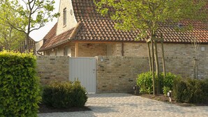 A stone building with a tiled roof, a gated entrance, and a cobblestone driveway. - B&B Het Weiland (Damme)