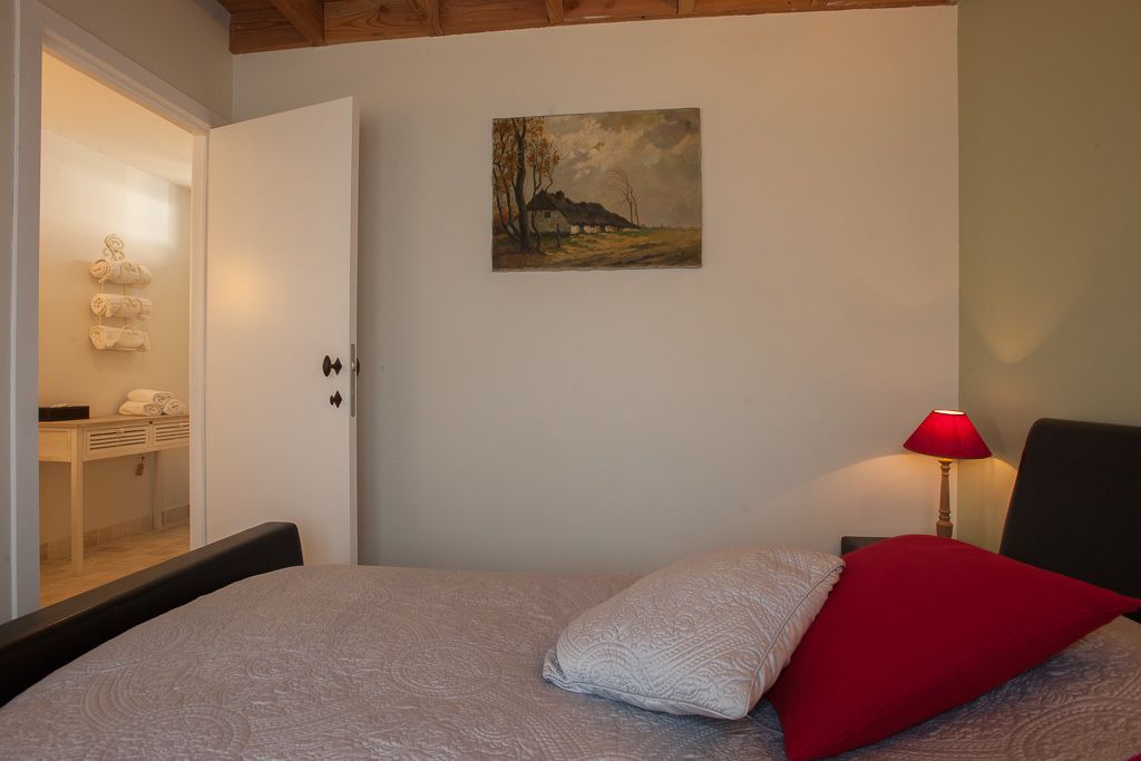 Ein Schlafzimmer mit einem Bett, einem Gemälde an der Wand, einer roten Lampe und einer Tür zu einem Badezimmer.