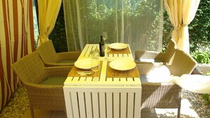 A dining area with wicker furniture, a table set for two, and a bottle of wine. - Forest&Sea apartment-Bikes&table incl (Medulin)