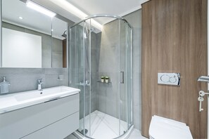 Een moderne badkamer met een glazen douchecabine, een witte wastafel en een wandpaneel van hout.