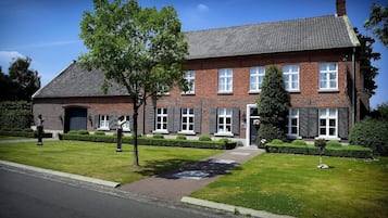 A two-story brick house with a sloped roof, a front door, and a small front yard with a lawn and a tree.