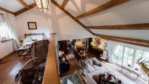 A spacious loft-style room with a high ceiling, exposed wooden beams, a large window with a view of greenery, a cozy seating area with a sofa and chairs, and a dining table set for two. - Casa Ciolina (Peer)