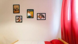 Une chambre à coucher avec un lit, des rideaux rouges et trois tableaux encadrés accrochés au mur.