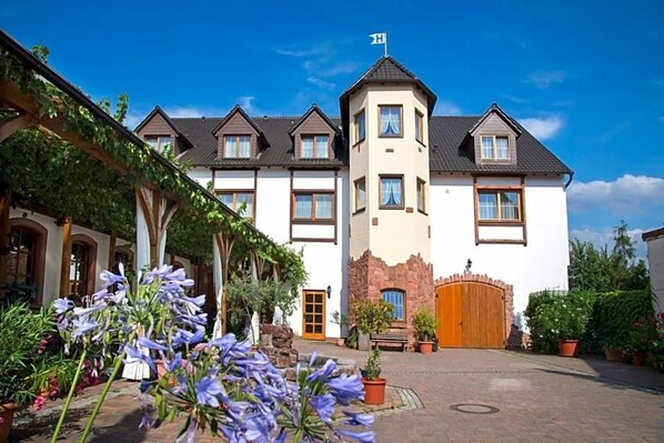 A hotel with a central tower, multiple windows, and a courtyard with potted plants.
