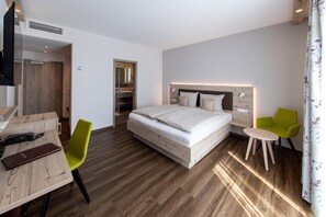 A hotel room with a wooden floor, a bed with white linens, a desk with a chair, and a small table with two chairs.
