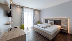 Un dormitorio moderno con una cama grande, un escritorio de madera, una silla y un televisor montado en la pared.