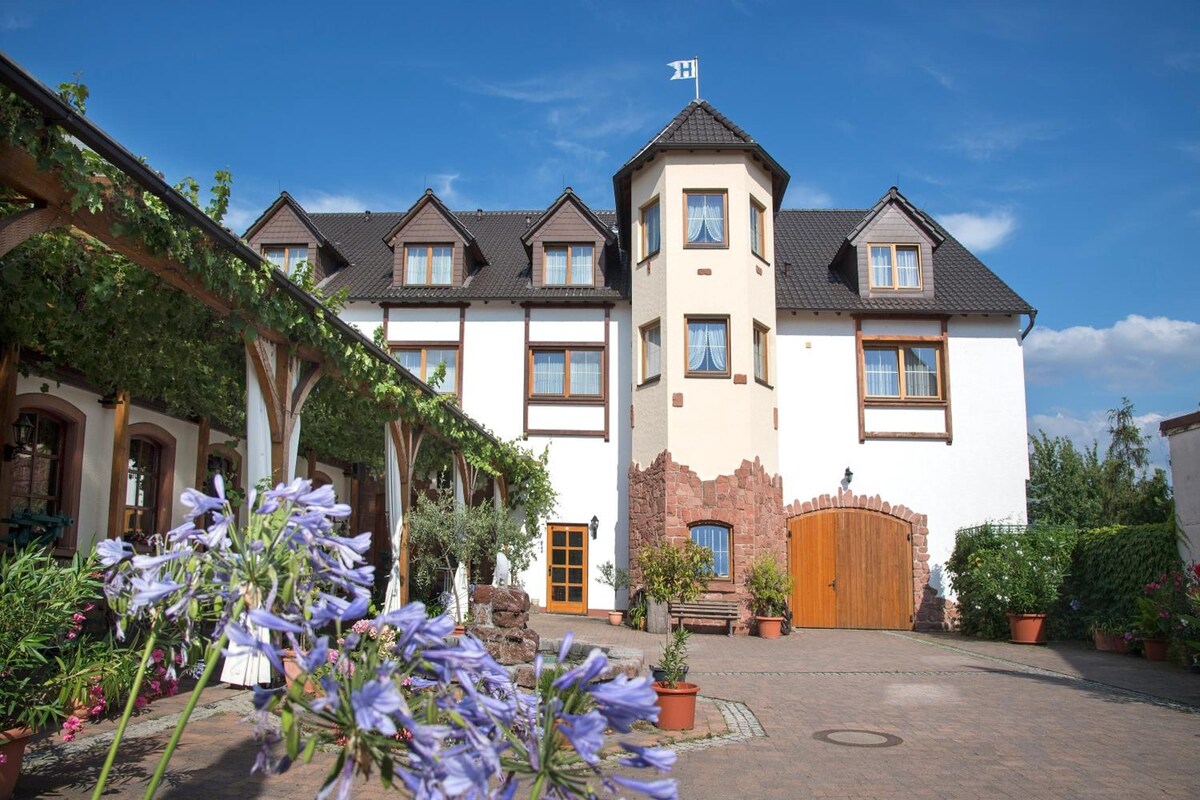 A large, multi-story hotel with a central tower, a covered courtyard with potted plants, and a flag on top of the tower.
