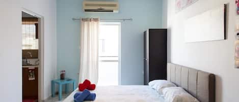 Un dormitorio con cama, una mesita, un armario y una ventana con cortinas.