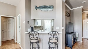 Une cuisine dotée d’un grand îlot central, de deux tabourets de bar, d’un élément décoratif représentant un poisson et d’un téléviseur.