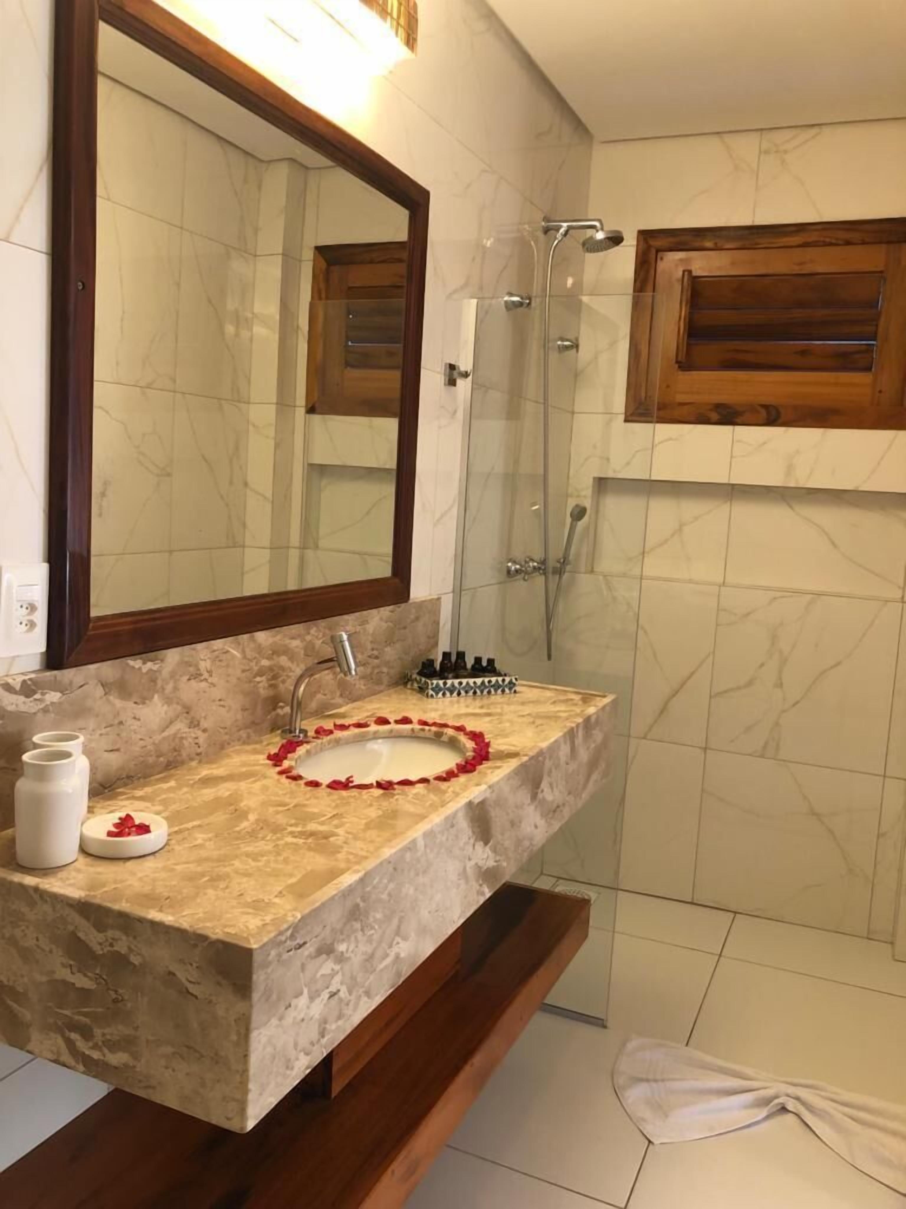 Een badkamer met een marmeren wastafel, een grote spiegel, een douche en houten kastjes.