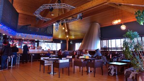 A spacious indoor dining area with high wooden ceilings, multiple tables and chairs, and a bar area with a variety of beverages. - VVF Lac Léman, Évian-les-Bains (Evian-les-Bains)