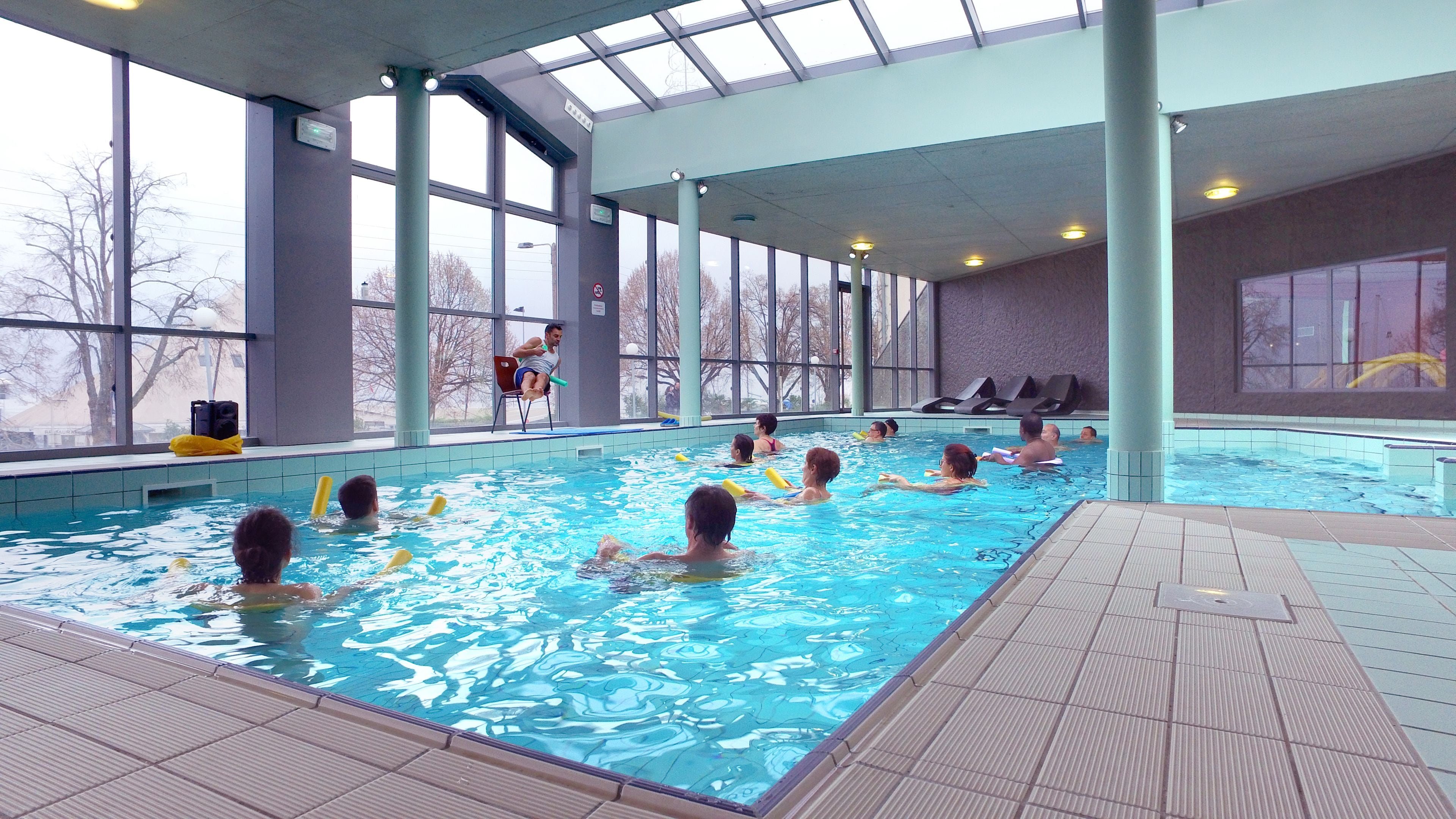 Ein Hallenbad mit klarem, blauem Wasser, großen Fenstern und einem gefliesten Boden.