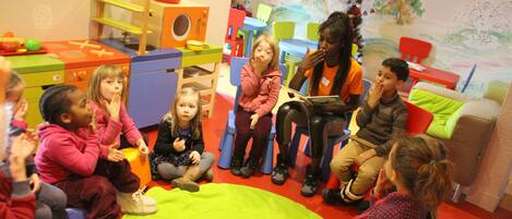 A group of children sitting on the floor in a room with colorful furniture and a mural on the wall.