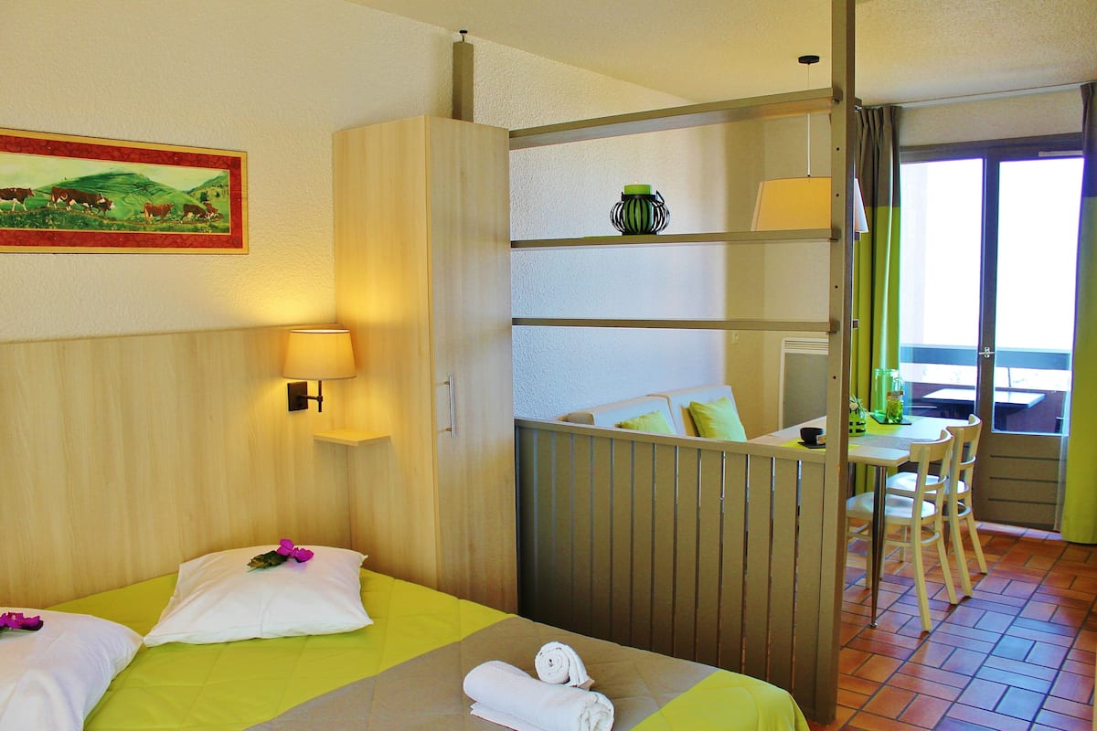 A hotel room with two beds, a dining area, and a view of the outdoors.