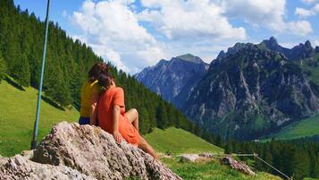 Eine bergige Landschaft mit einer Fahnenstange und zwei Personen, die auf einem Felsen sitzen.