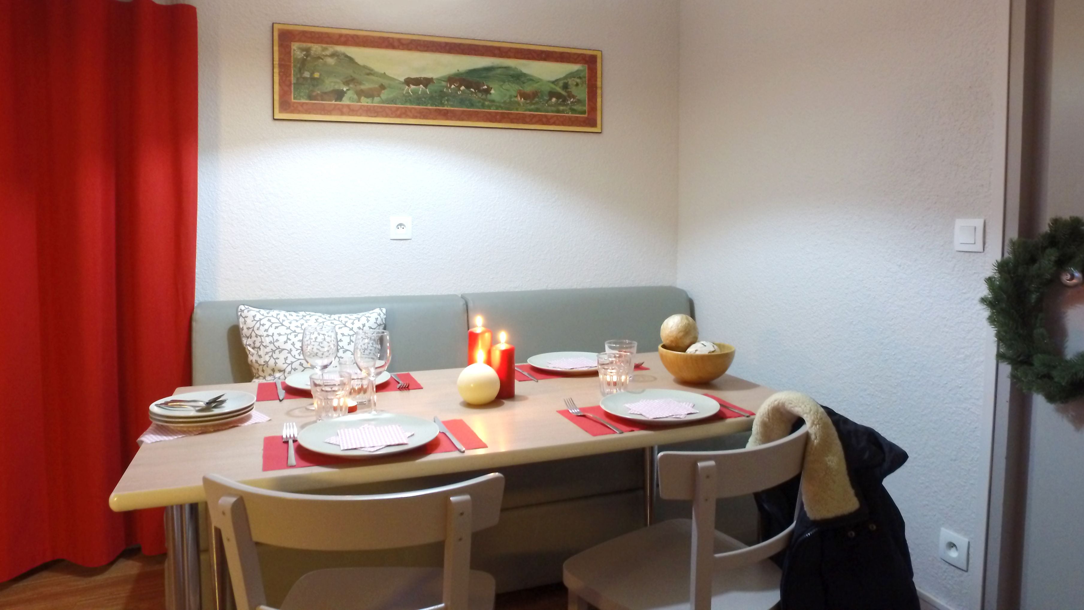Un coin repas avec une table mise pour deux, agrémentée d’un chandelier servant de centre de table, d’assiettes, de verres et de couverts. Un tableau est accroché au mur, au-dessus de la table.