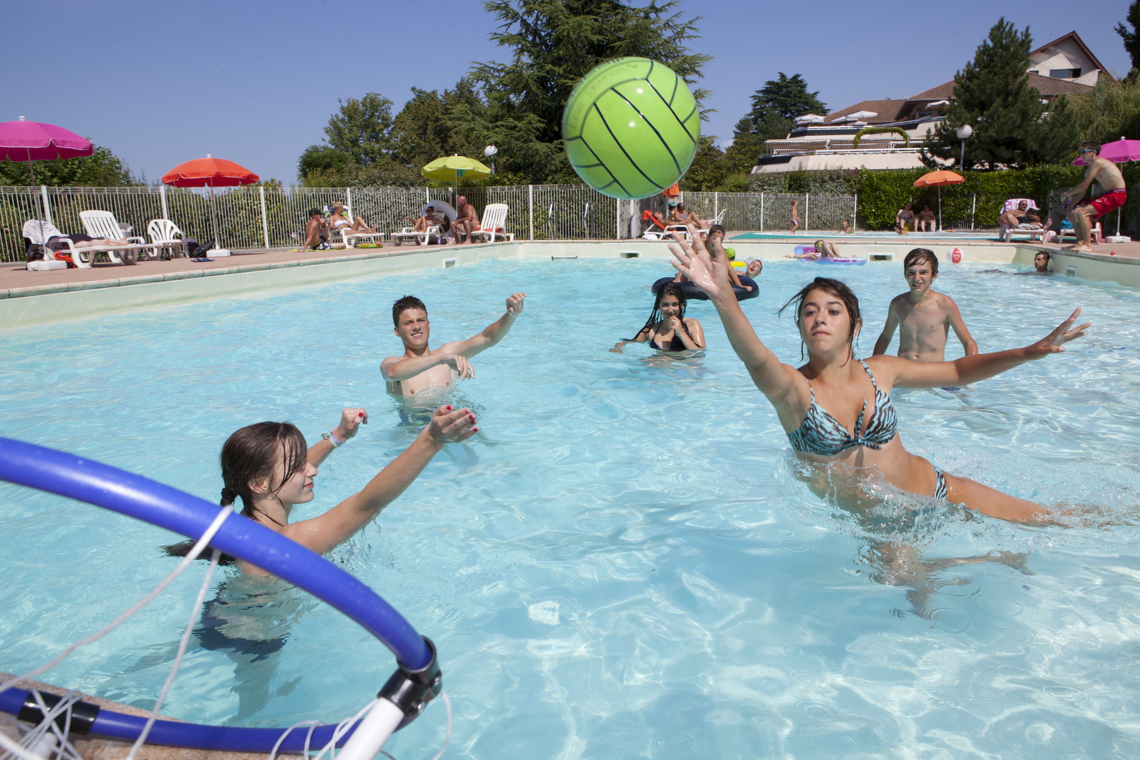 A swimming pool with people playing volleyball.