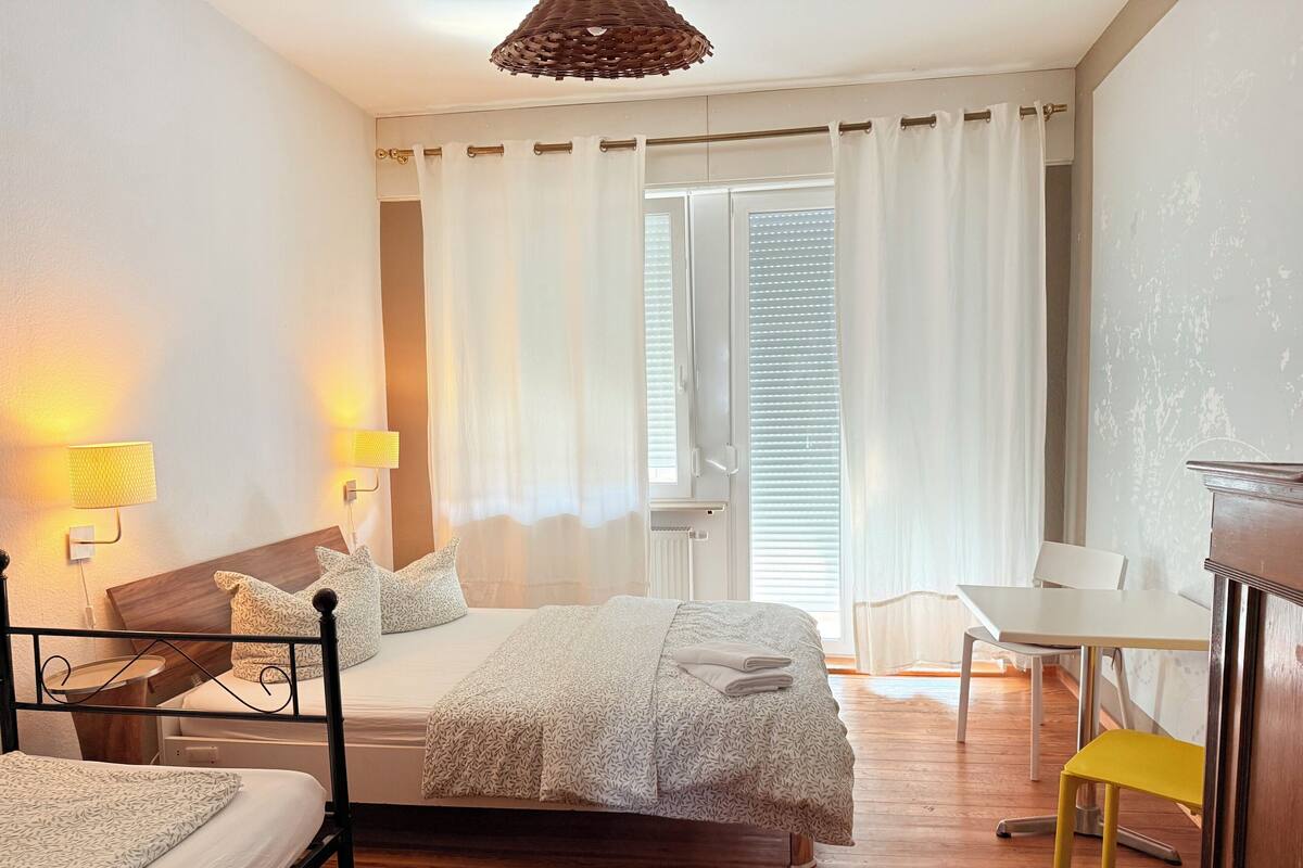 A bedroom with a bed, bedside tables, a desk, a chair, and a window with curtains.