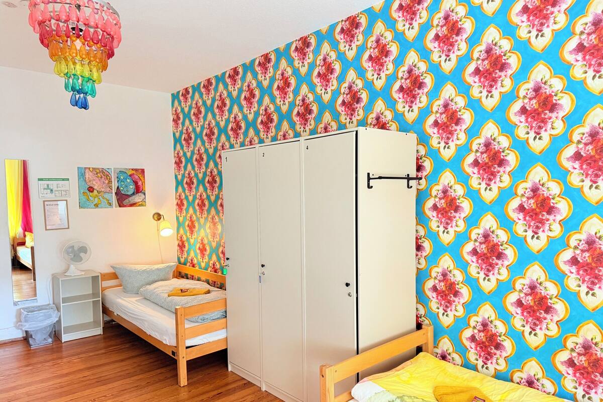 A room with a bunk bed, a wardrobe, a fan, and a colorful floral wallpaper.