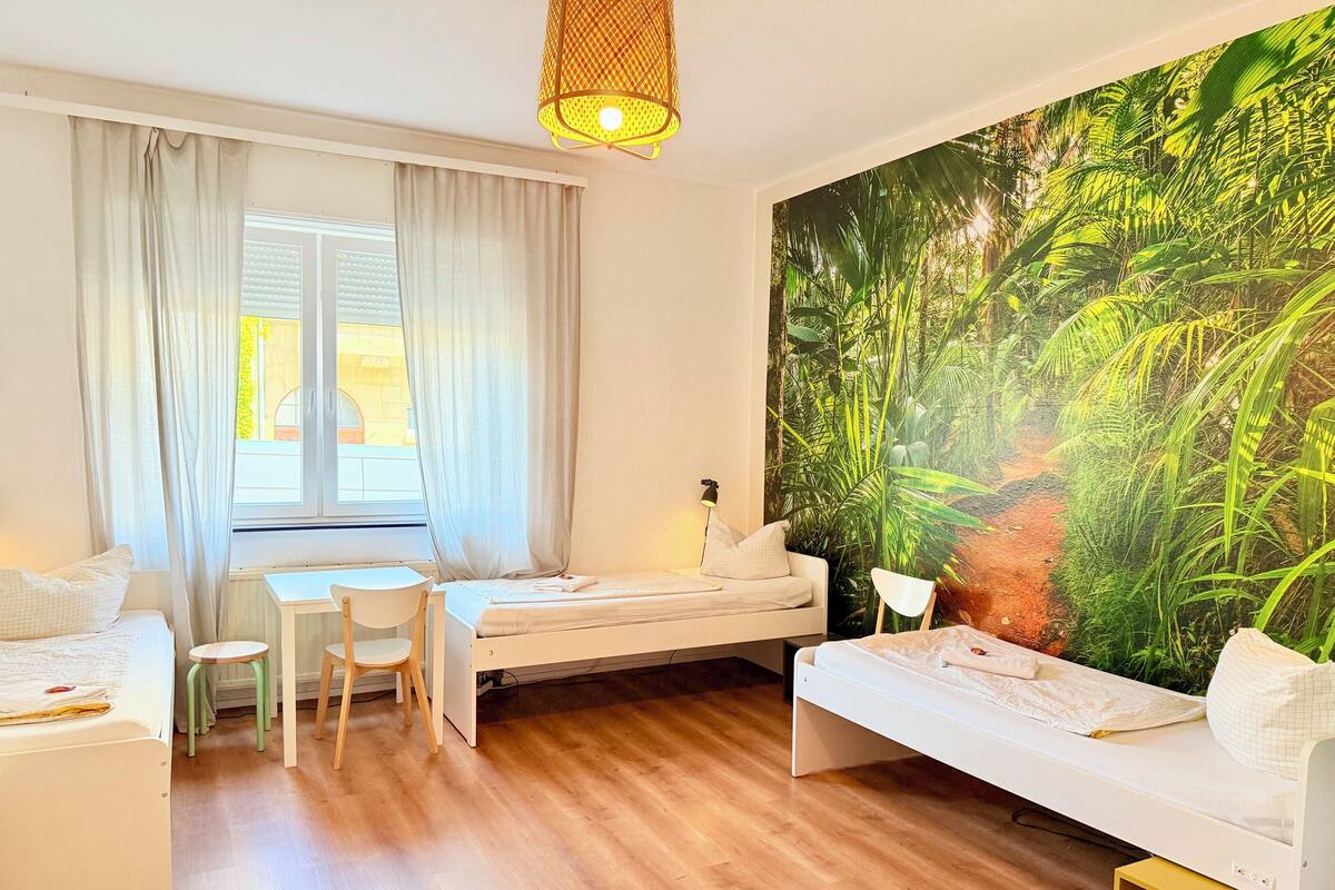 A room with a bed, a desk, a chair, and a large wall mural of a forest.
