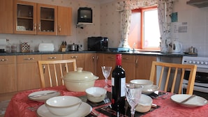 Una cocina con armarios de madera, microondas, estufa y una mesa de comedor con platos, tazones y una botella de vino.