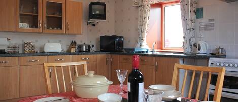 A kitchen with wooden cabinets, a microwave, a stove, and a dining table set with plates, bowls, and a wine bottle.