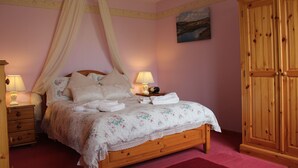 Un dormitorio con cama con dosel, una mesita de noche con lámpara, un armario de madera y un cuadro en la pared.