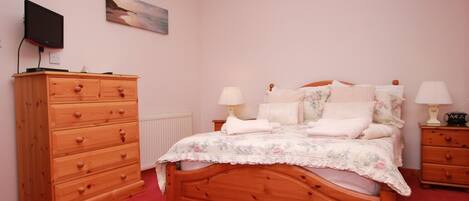 A bedroom with a wooden bed, two bedside tables with lamps, a wooden dresser, and a painting on the wall.