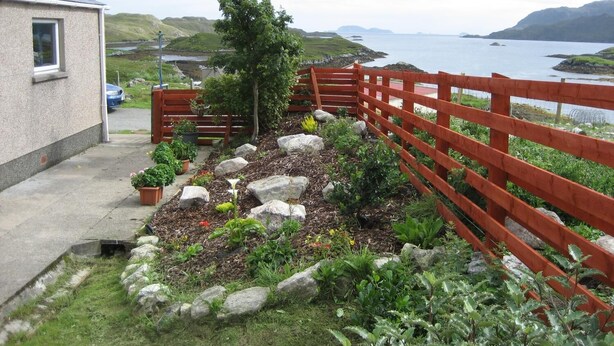 Un jardín con cerca de madera, plantas en macetas y vista al mar.