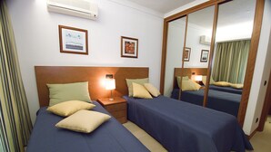 Habitación de hotel con dos camas, una mesita de noche con lámpara, un espejo y cuadros en la pared.