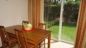 Un área de comedor con una mesa y sillas de madera, una cesta de fruta y vistas de un jardín a través de un ventanal.