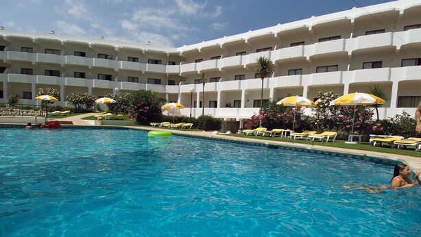 Zona de piscina de hotel con agua cristalina, tumbonas y sombrillas.