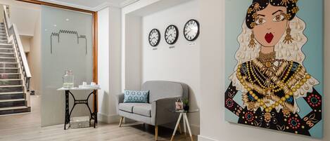 A modern living room with a grey sofa, a small table with a glass jar, and three wall clocks.