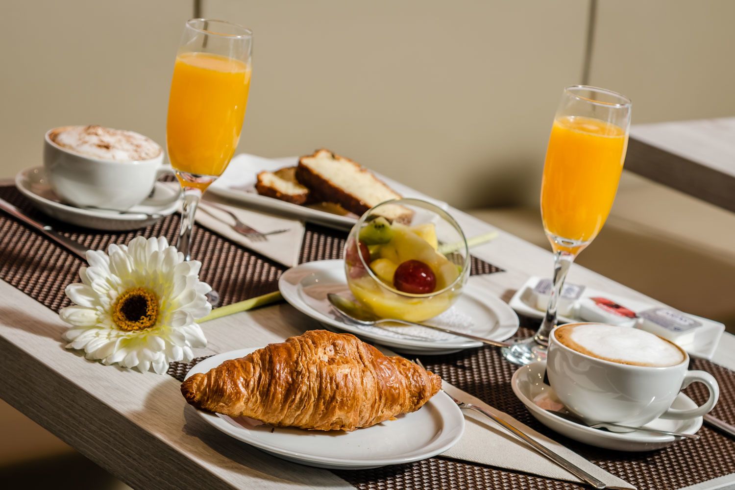 A breakfast setting with croissants, fruit salad, orange juice, and coffee on a table.