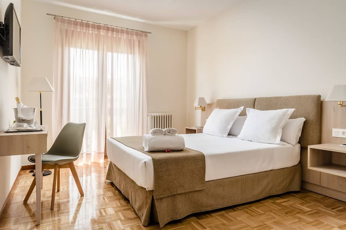 A hotel room with a bed, a desk, a chair, a TV, and a window with curtains.