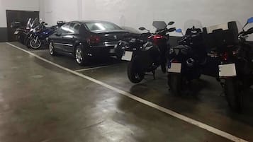 A parking garage with a black car and several motorcycles parked in rows.
