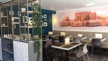 A modern cafe with a glass partition, seating area, and a wall with wine corks.