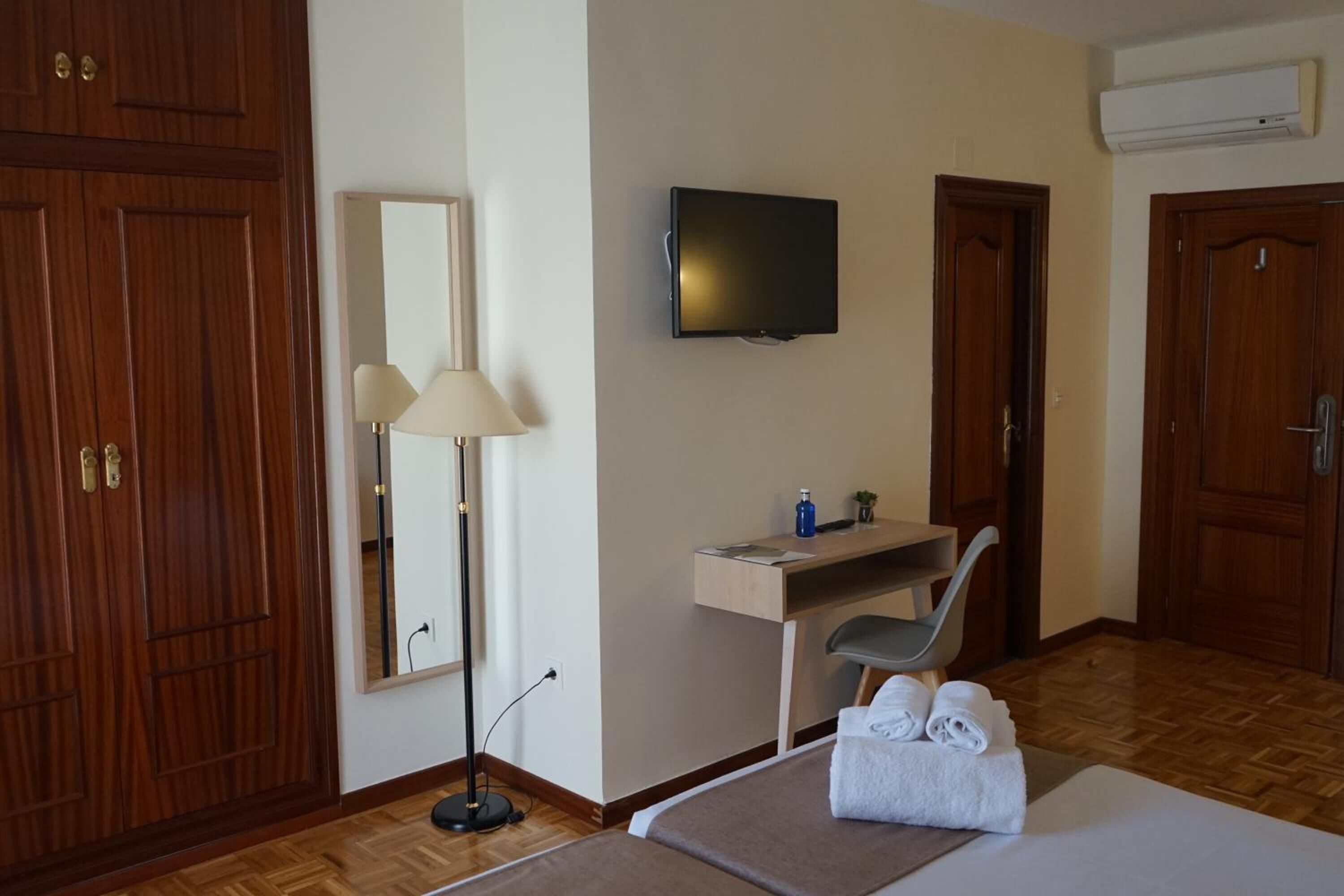 Une chambre d’hôtel comprenant un lit, un bureau avec une chaise, un téléviseur à écran plat, un miroir et des portes en bois.