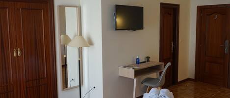 Une chambre d’hôtel comprenant un lit, un bureau avec une chaise, un téléviseur à écran plat, un miroir et des portes en bois.