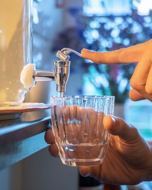 A hand holding a glass under a water tap, with water flowing into it. - The Restel - Hostel (Chiang Mai)