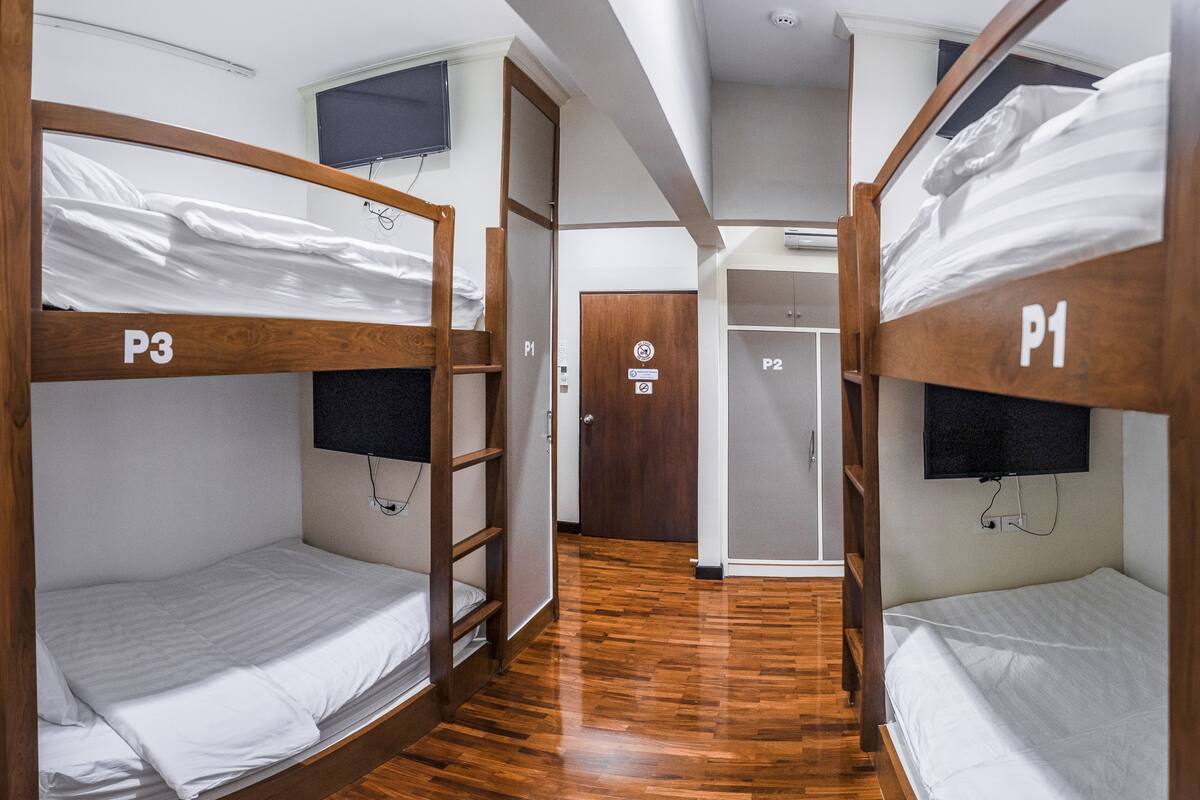 A hotel room with bunk beds labeled P1, P2, P3, and P4, wooden flooring, and a door with a P2 sign.