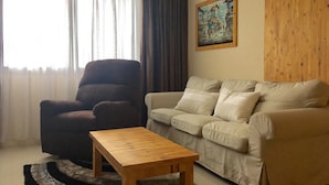 Een woonkamer met een bruine fauteuil, een beige bank en een houten salontafel.