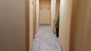 A hallway with a light-colored tiled floor, wooden doors, and a potted plant.