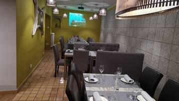 A restaurant with a long dining table set for a meal, multiple chairs, and a projection screen on the wall.