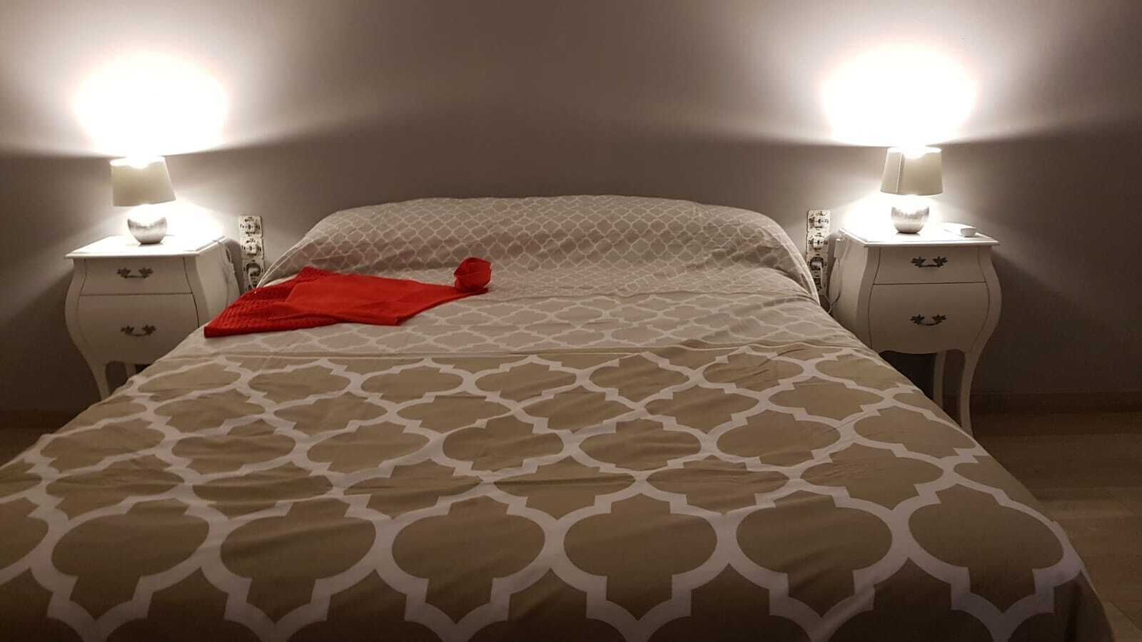 A neatly made bed with a patterned bedspread, two bedside tables with lamps, and a red throw blanket on the bed.