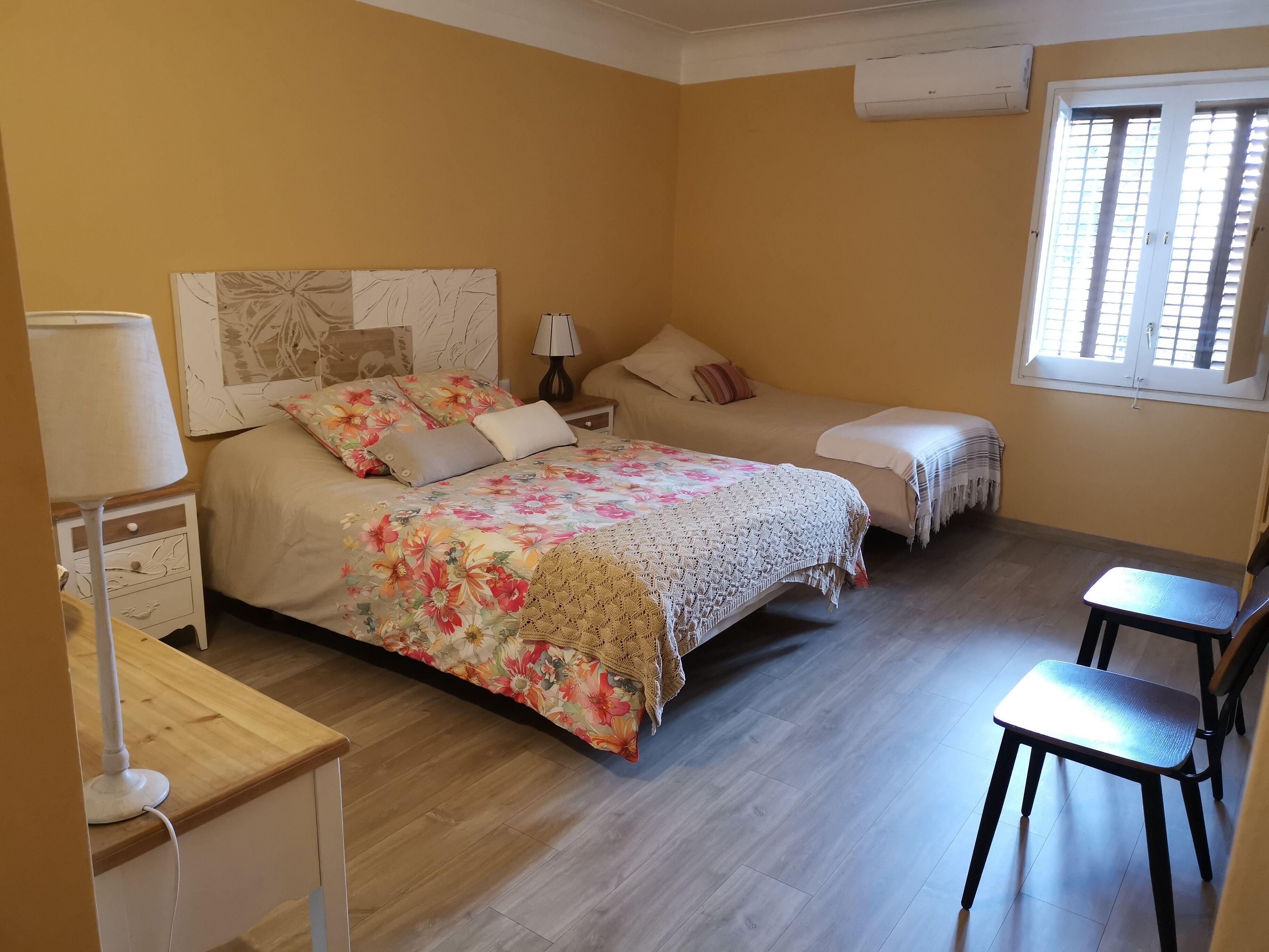 Un dormitorio con dos camas, una mesita de noche con lámpara, una silla y una ventana con persianas.