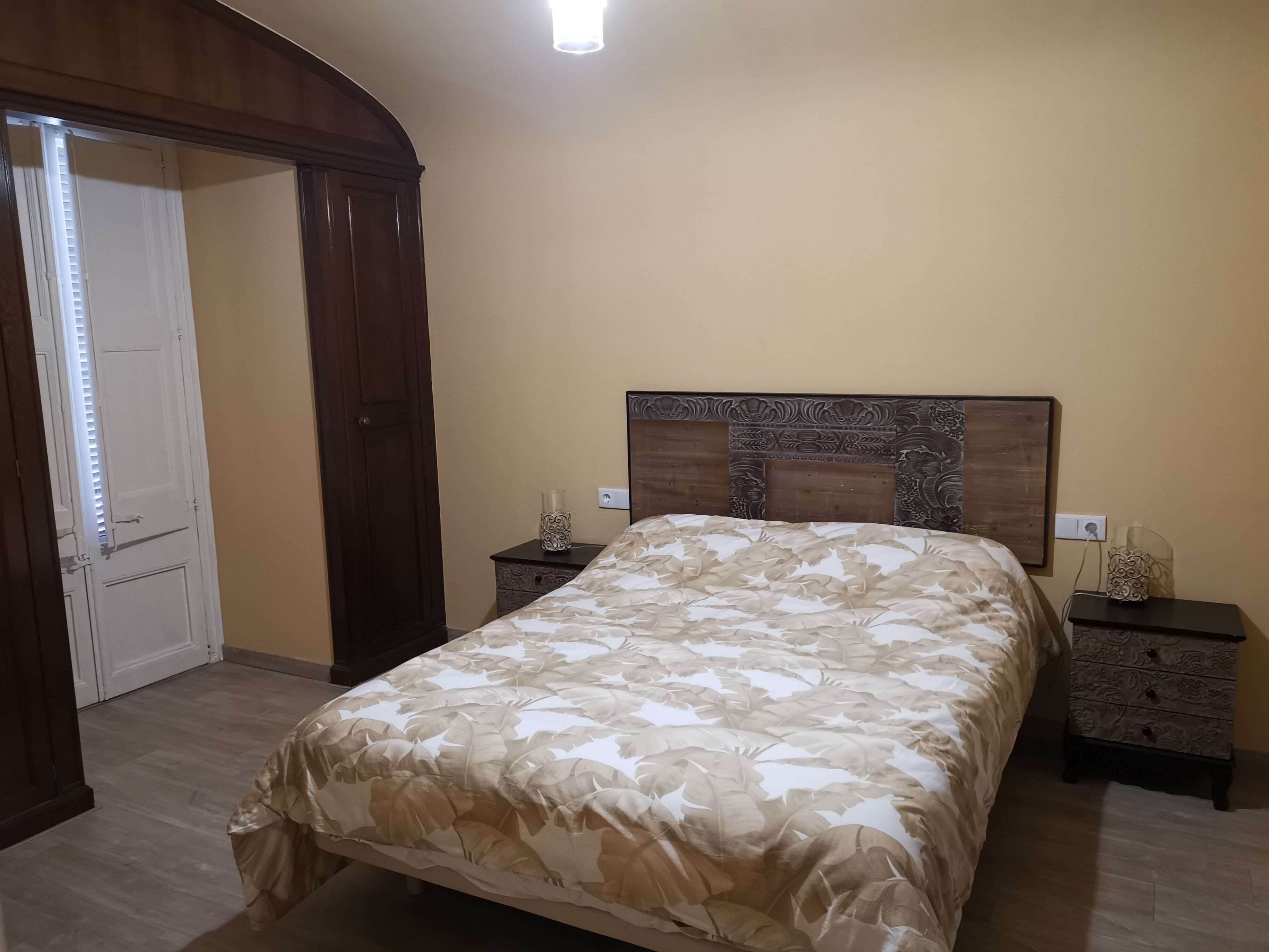 Quarto com uma cama, duas mesas de cabeceira, um painel de madeira e uma porta com persianas.